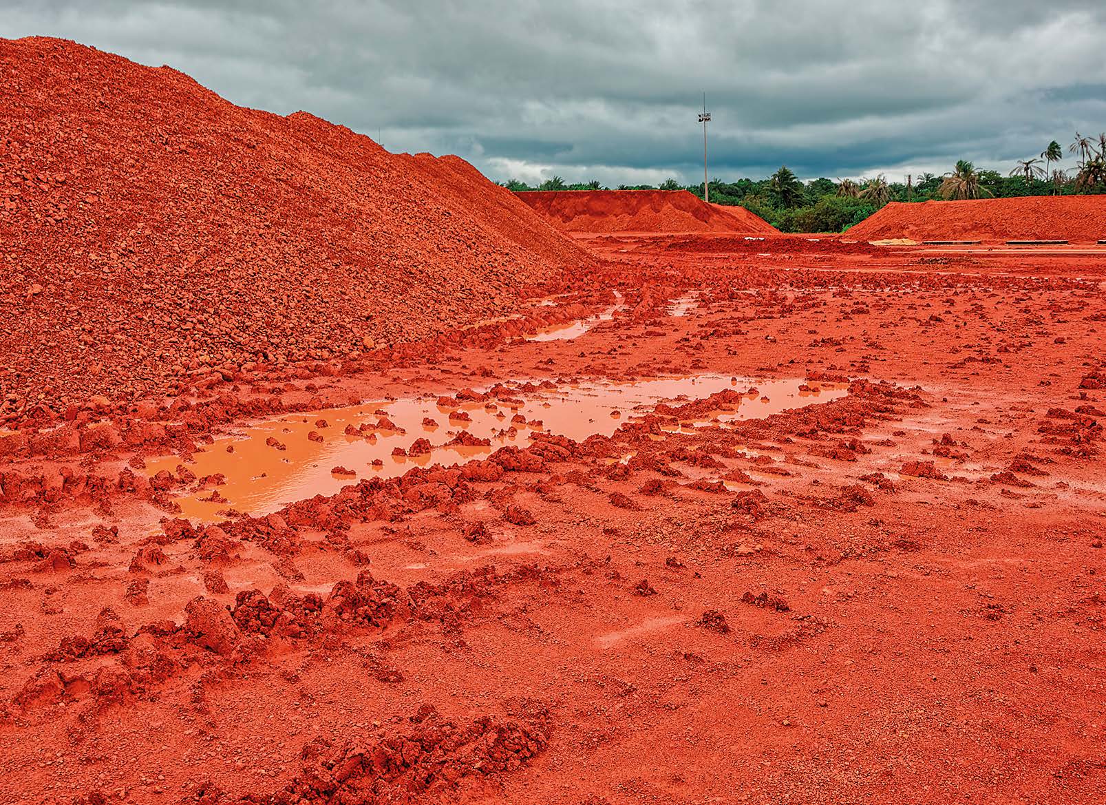 Rødt mineaffald fra bauxit-produktion i Guinea, Vestafrika. Store bunker af rød jord strækker sig ud over landskabet under en overskyet himmel