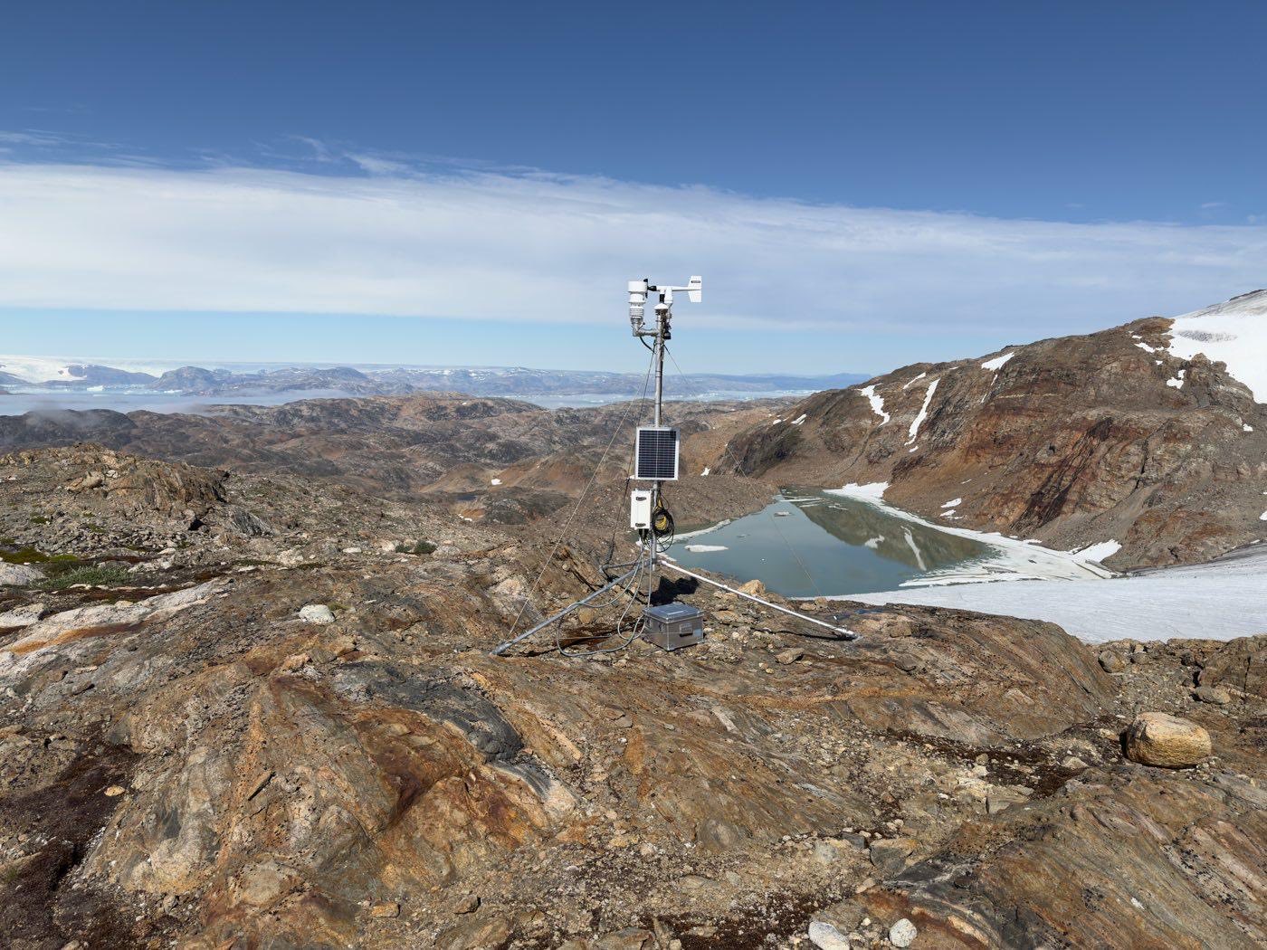 PROMICE-vejrstationen på klippen ved Mittivakkat-gletsjeren med gletsjersø i baggrunden